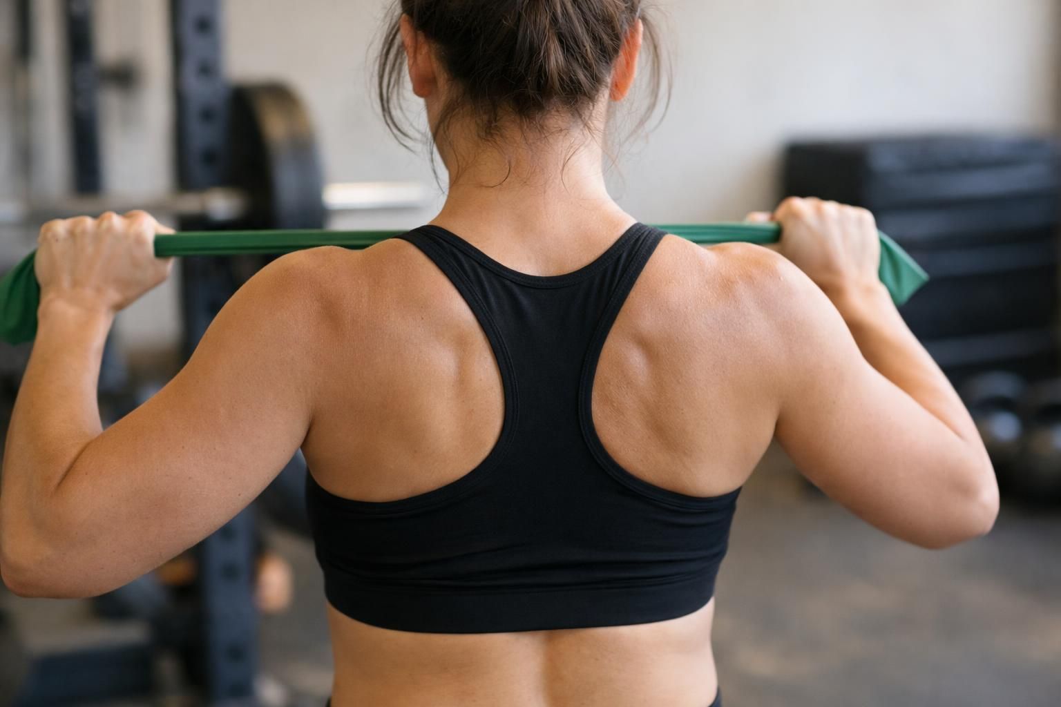 Woman in black sports bra stretching green resistance band