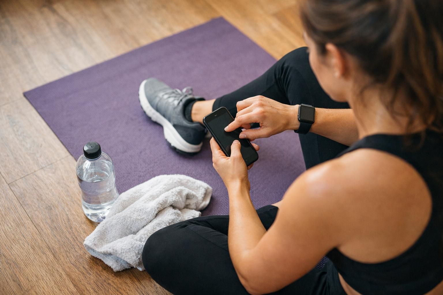 Woman on purple yoga mat checking phone beside towel