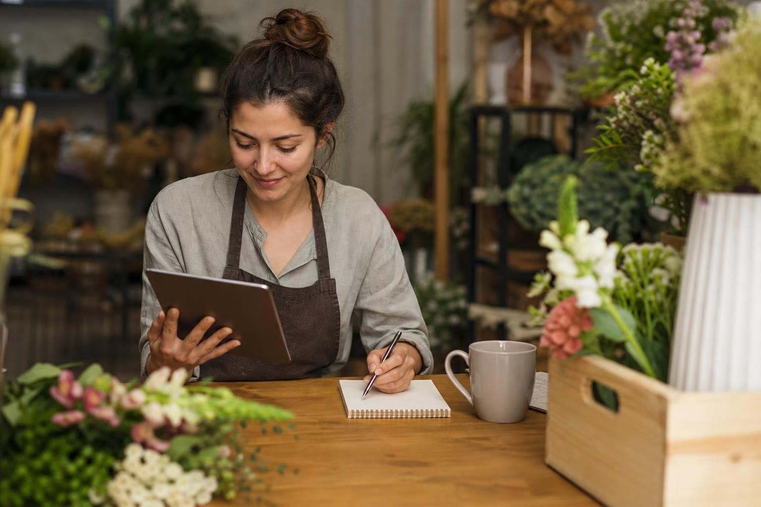 Florist checks tablet and writes notes beside flowers
