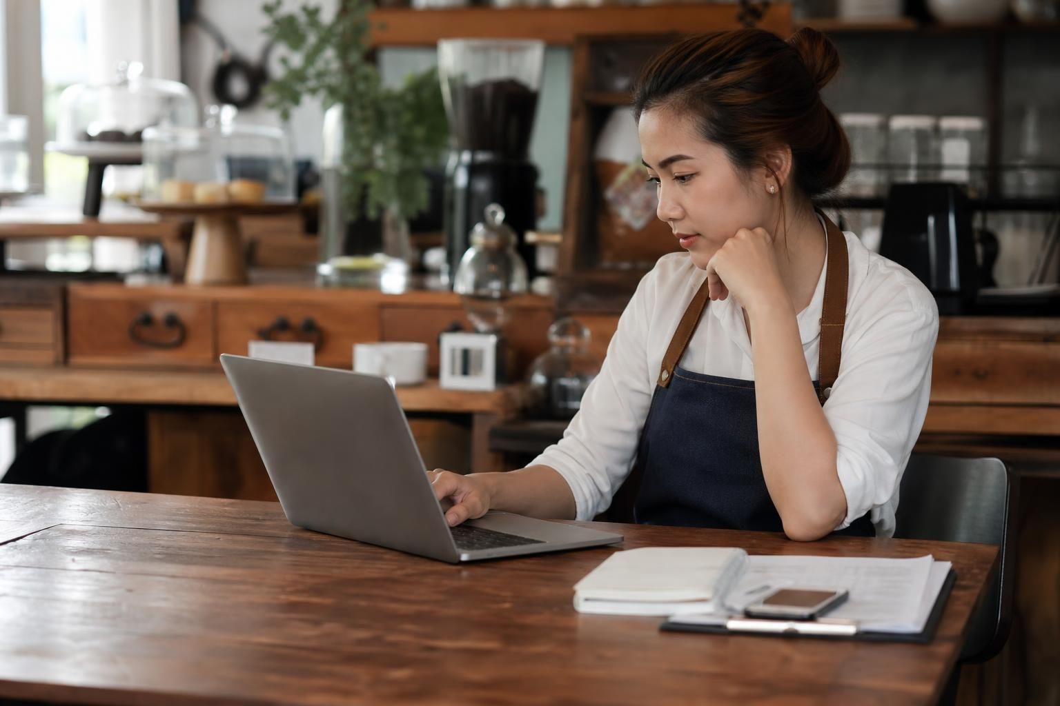 Cafe owner reviews laptop beside notebook and phone